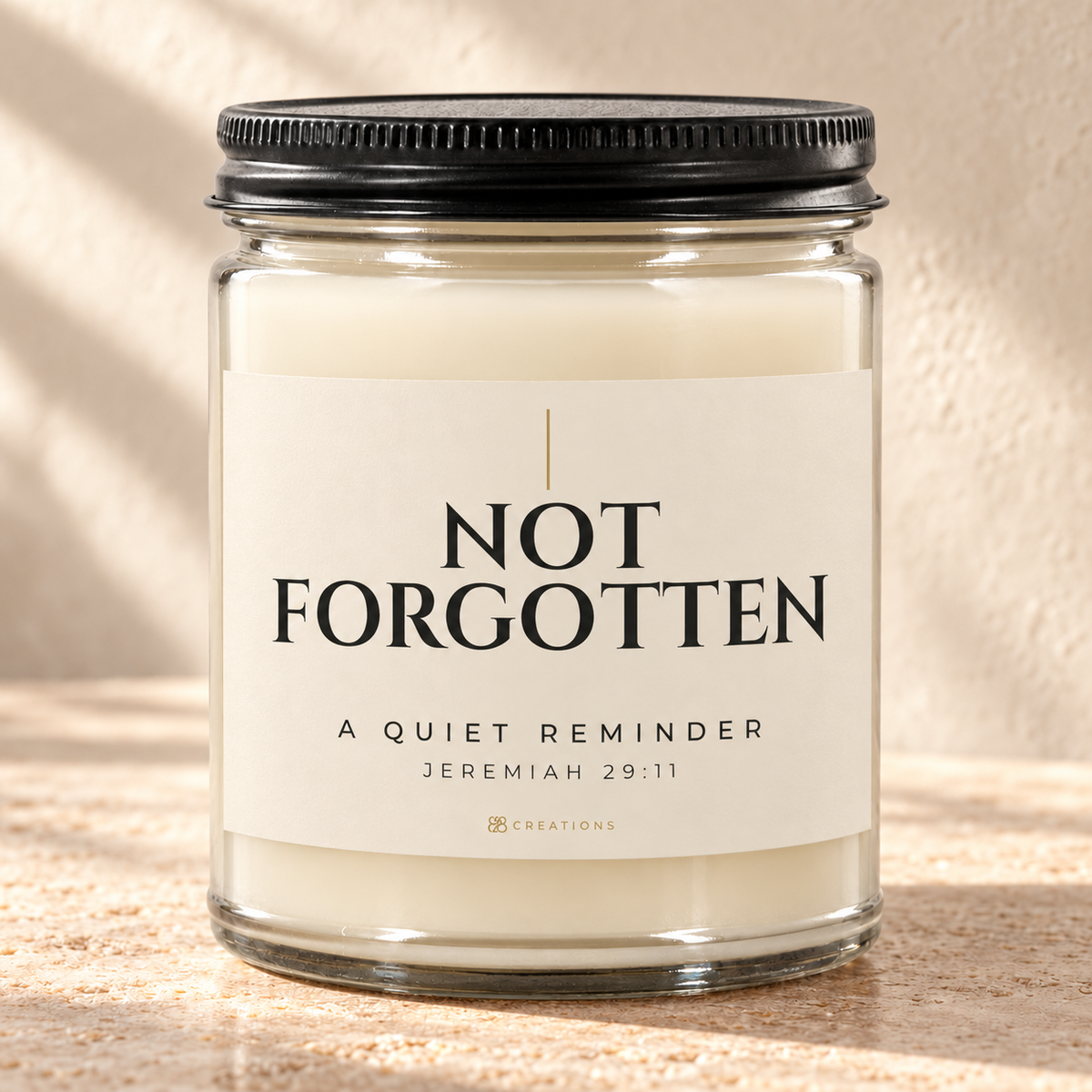 828 Creations NOT FORGOTTEN Jeremiah 29:11 Sea Breeze candle in Bone, with a clear glass jar and ribbed black lid, styled in warm sunlight.