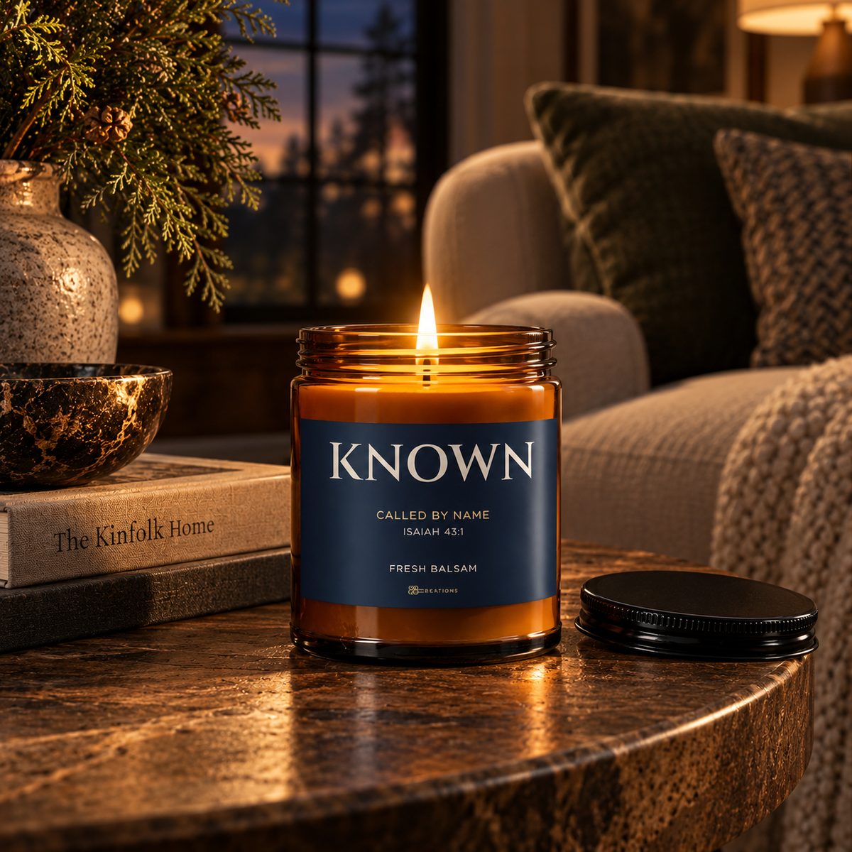 Lit KNOWN Isaiah 43:1 Fresh Balsam candle by 828 Creations on a living-room table, with its black lid beside the amber jar and navy label. Digital promotional mockup.
