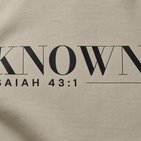 Simulated detail mockup of charcoal KNOWN. and Isaiah 43:1 transfer artwork on Stone fleece; not a manufactured sample photograph.