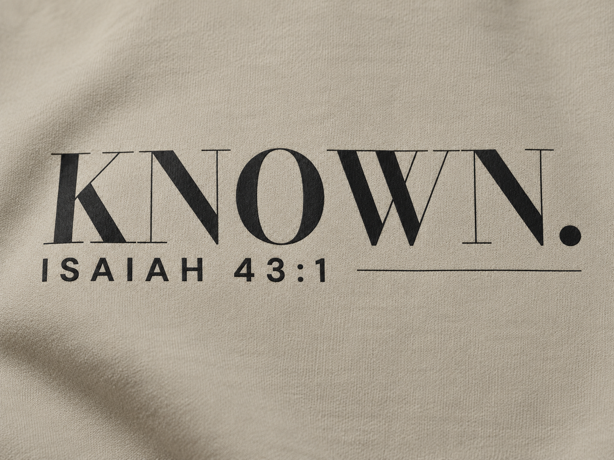 Simulated detail mockup of charcoal KNOWN. and Isaiah 43:1 transfer artwork on Stone fleece; not a manufactured sample photograph.