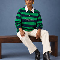 Green and navy rugby polo styled with ecru trousers and black boots in a seated studio editorial