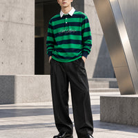 Green and navy rugby polo styled with wide black pleated trousers and leather shoes beside modern architecture