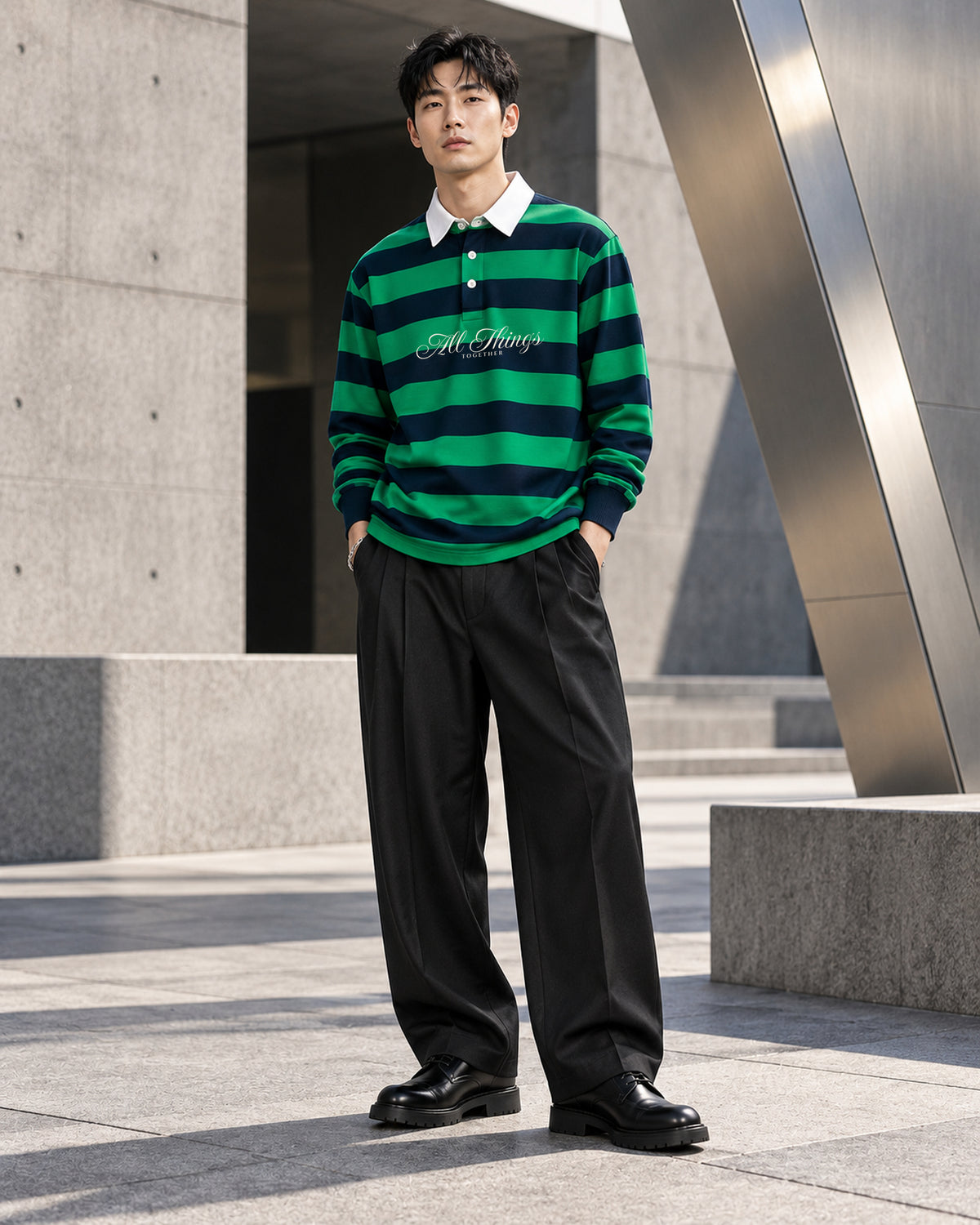 Green and navy rugby polo styled with wide black pleated trousers and leather shoes beside modern architecture