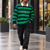 Green and navy rugby polo styled with dark denim and cream sneakers in a modern shopping district