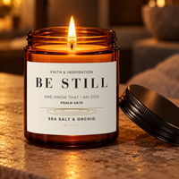 Lit BE STILL Psalm 46:10 Sea Salt & Orchid candle with the matching ribbed black lid beside the amber jar.