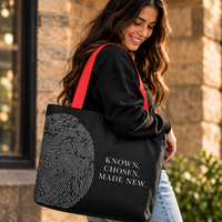 Woman carrying the black Believer Identity large tote with red handles and Known. Chosen. Made New. fingerprint design