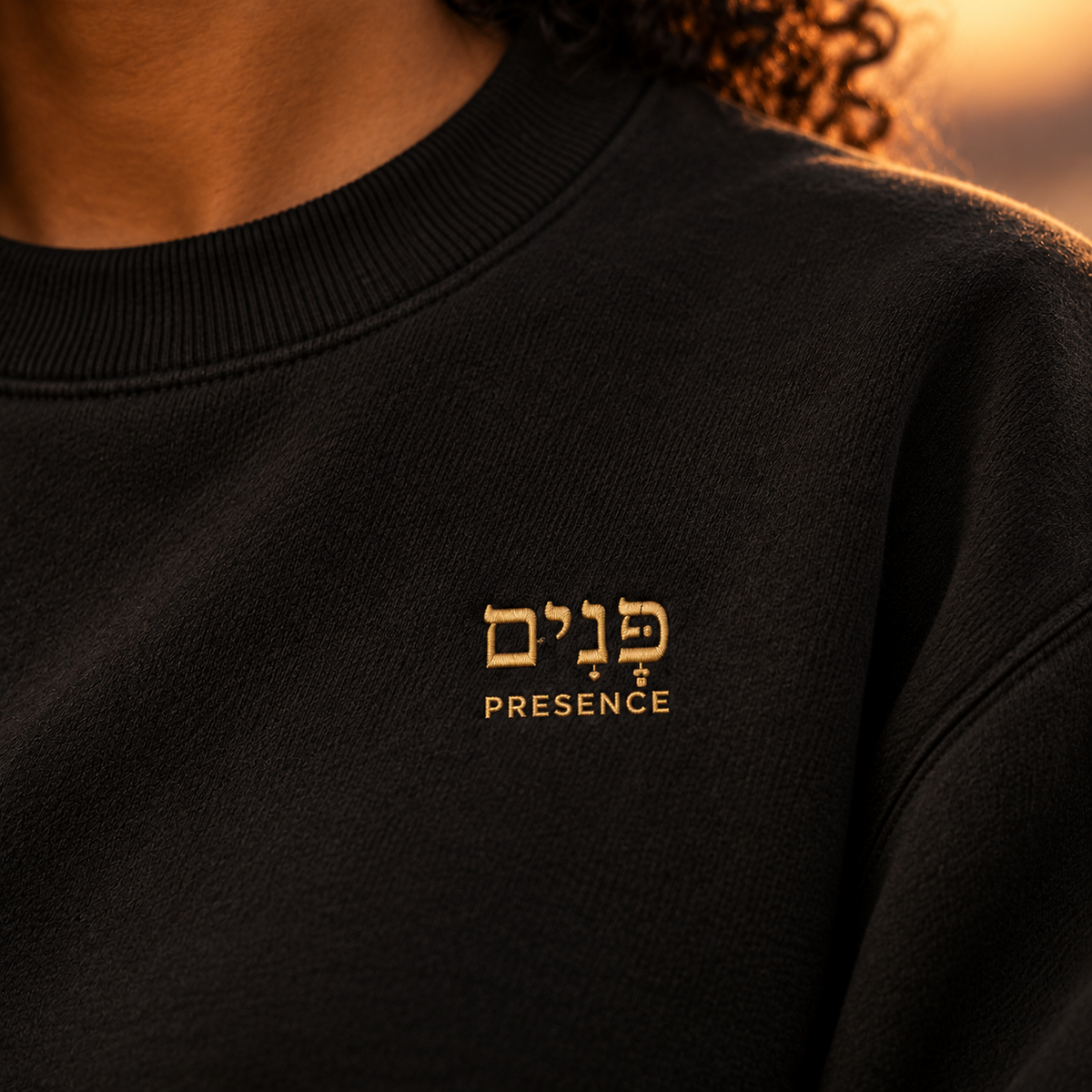 Close-up of the black sweatshirt showing the gold embroidered Hebrew word Panim with the word “Presence” stitched underneath.