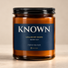 828 Creations KNOWN Isaiah 43:1 Fresh Balsam candle in amber glass with a midnight-navy label and fine-ridged black lid on a neutral background.