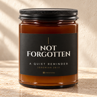 828 Creations NOT FORGOTTEN Jeremiah 29:11 Charcoal candle in amber glass with a matte black ribbed lid, styled on warm stone with the approved smaller title and tiny maker mark.