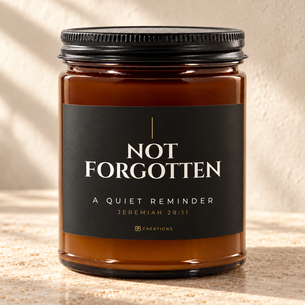 828 Creations NOT FORGOTTEN Jeremiah 29:11 Charcoal candle in amber glass with a matte black ribbed lid, styled on warm stone with the approved smaller title and tiny maker mark.