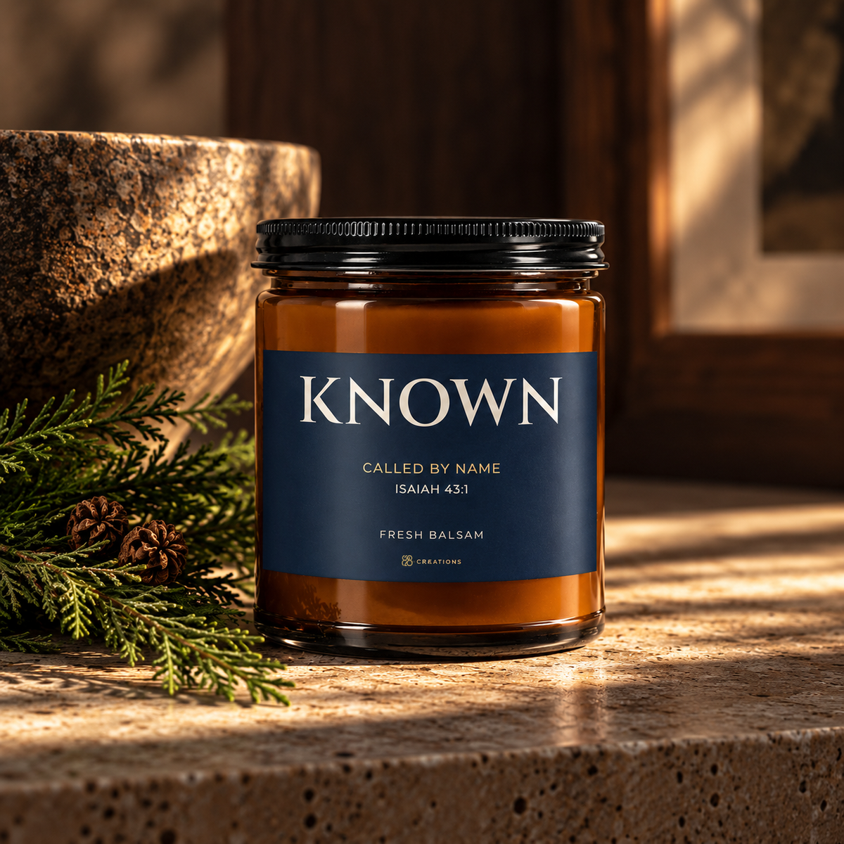 KNOWN Fresh Balsam scripture candle by 828 Creations, with amber glass and a navy Isaiah 43:1 label, styled beside evergreen branches in warm natural light.