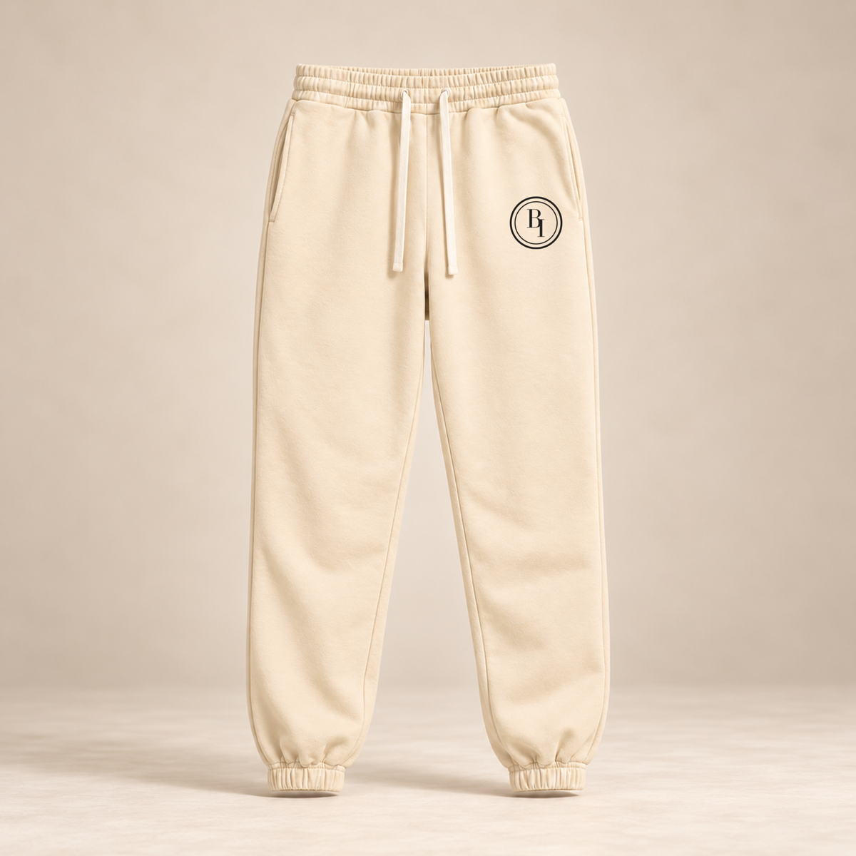 BELIEVER IDENTITY Cream Apricot Essential Sweatpants with Black BI emblem front view