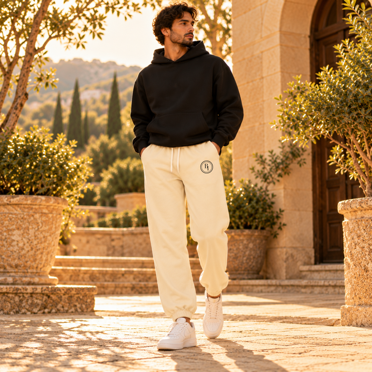 Man wearing BELIEVER IDENTITY Cream Apricot sweatpants with Black BI emblem and black hoodie